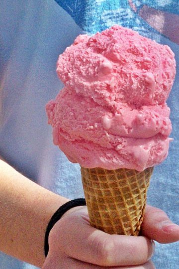 Pink lemonade ice cream in a cone being held