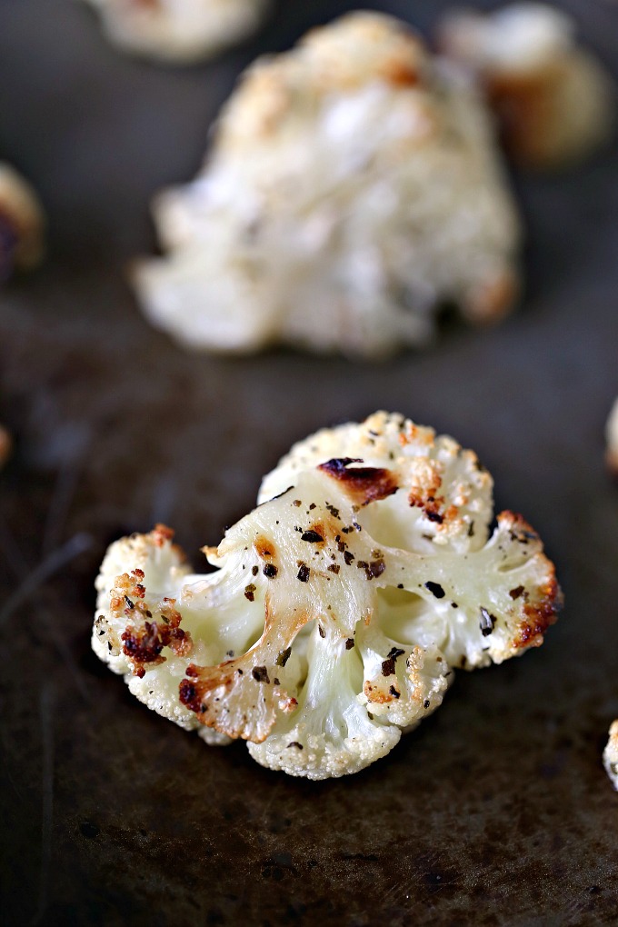 close up image of roasted cauliflower on a dark cookie sheet 