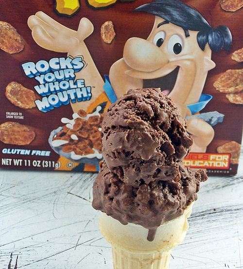 Cocoa pebbles ice cream served in a cone with box of cereal in the background