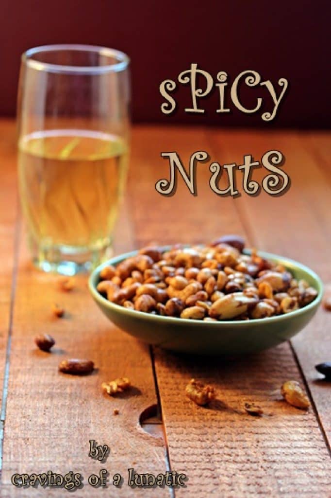 A bowl of spicy nuts next to a glass of beer on a wooden surface.