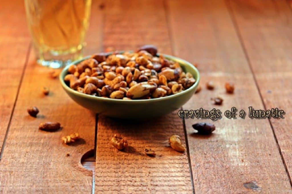 A bowl of spicy nuts with a glass of beer nearby.