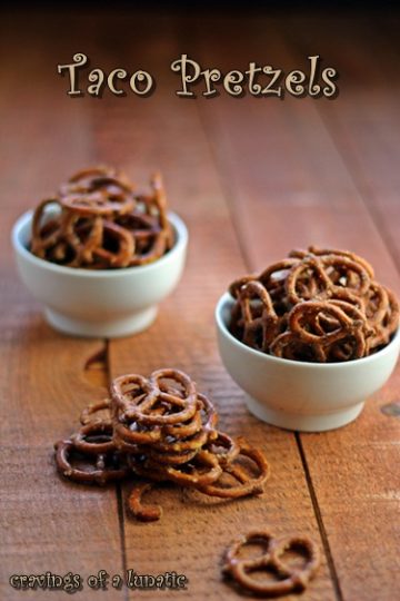 slow cooker taco seasoned pretzels in white bowls on a wood table with pretzels in a pile for snacking on