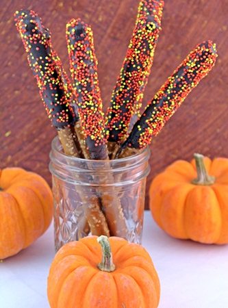 pretzels dipped in chocolate and sprinkles and stashed in a mason jar surrounded by mini pumpkins