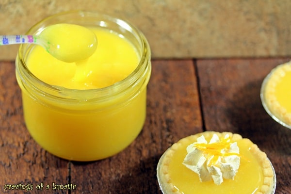 Mini Meyer Lemon Pies on wood surface with a jar of lemon curd in the background.