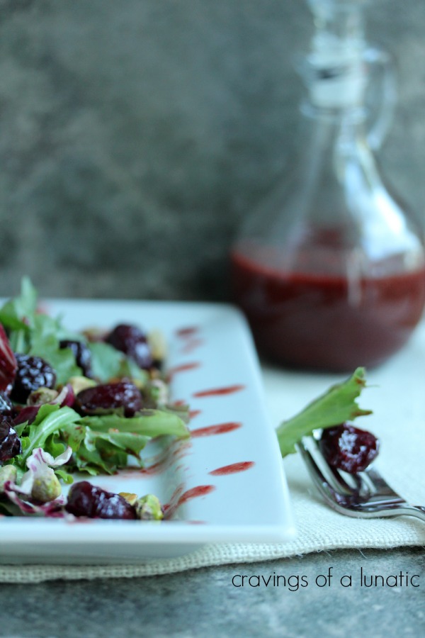 Roasted Cherry and Pistachio Salad with Roasted Cherry Vinaigrette served on a white plate with a glass jar in the background with extra vinaigrette in it