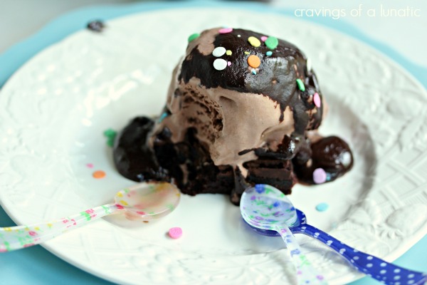 Brownie explosion ice cream sundae on a white plate with multi coloured spoons resting on the plate. Coloured confetti sprinkles are on top of the sundae.