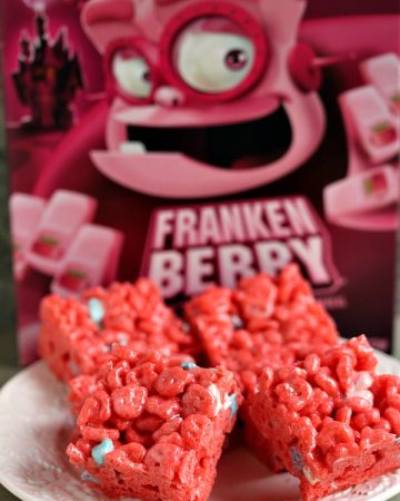 Franken Berry Krispies on a white plate with a box of the monster cereal behind it