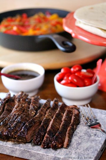 steak fajitas sliced on a grey board with all the other ingredients on table behind it