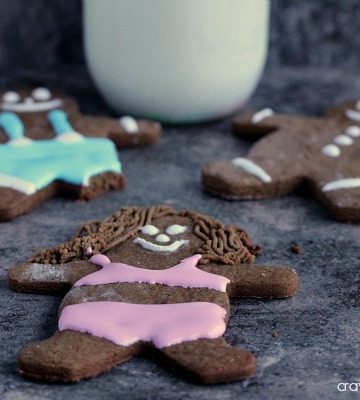 gingerbread people decorated on a dark counter with a glass of milk nearby