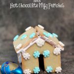Mini Sugar Cookie Houses Hot Chocolate Mug Perches on a dark counter.