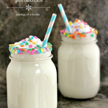 Slow cooker white chocolate hot chocolate served in mason jars with sprinkles on the rim and straws inside the glasses.