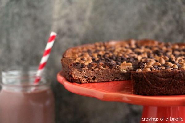 Peanut butter and chocolate brownies on a coral cake stand with a drink in the background.