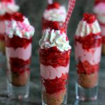 fun, brightly colored image of Strawberry Shortcake No Bake Mini Cheesecakes served layered in tall shot glasses with brightly colored spoons