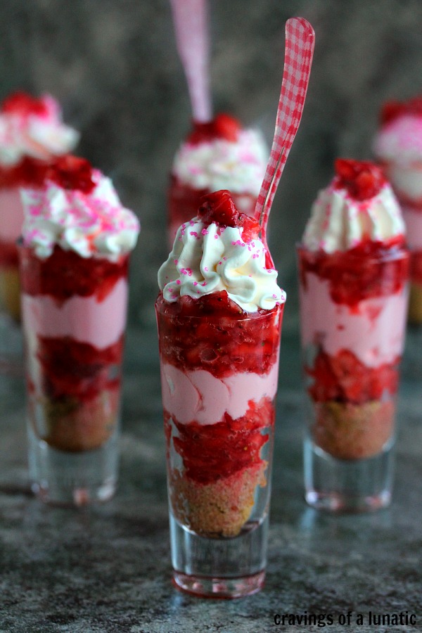 fun, brightly colored image of Strawberry Shortcake No Bake Mini Cheesecakes served layered in tall shot glasses with brightly colored spoons