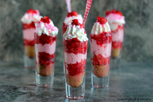 horizontal image of Strawberry Shortcake No Bake Mini Cheesecakes served layered in tall shot glasses with brightly colored spoons