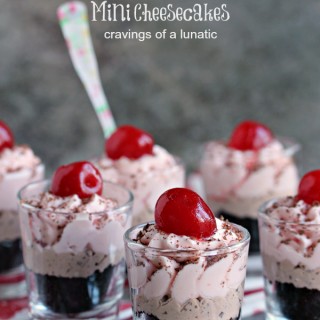 No bake cherry and chocolate chip cheesecake layered in shot glasses with a cherry on top and spoon in some glasses. Shot glasses are sitting on a red and white napkin with a dark background.