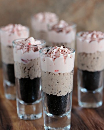 No bake cherry and chocolate cheesecakes layered in tall shot glasses sitting on a wood board.
