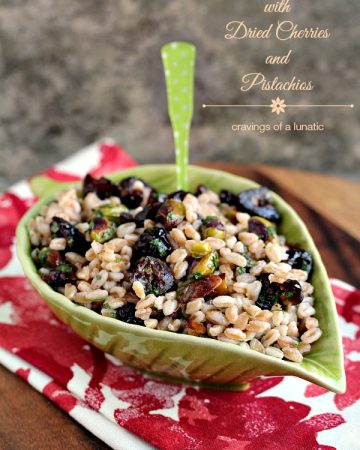 Farro with Pistachios and Dried Cherries served in a green leaf shaped bowl on a red and white napkin.
