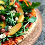 Pizza with Arugula, Peaches and Hazelnuts served on a wooden board