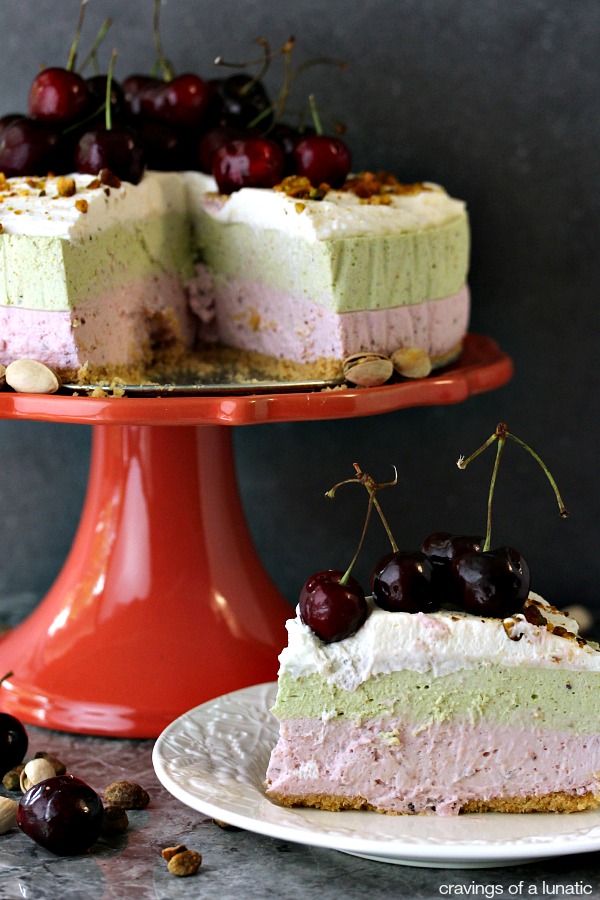 No Bake Cherry and Pistachio Cheesecake with Animal Cracker Crust sliced and placed on plate with cake stand in background