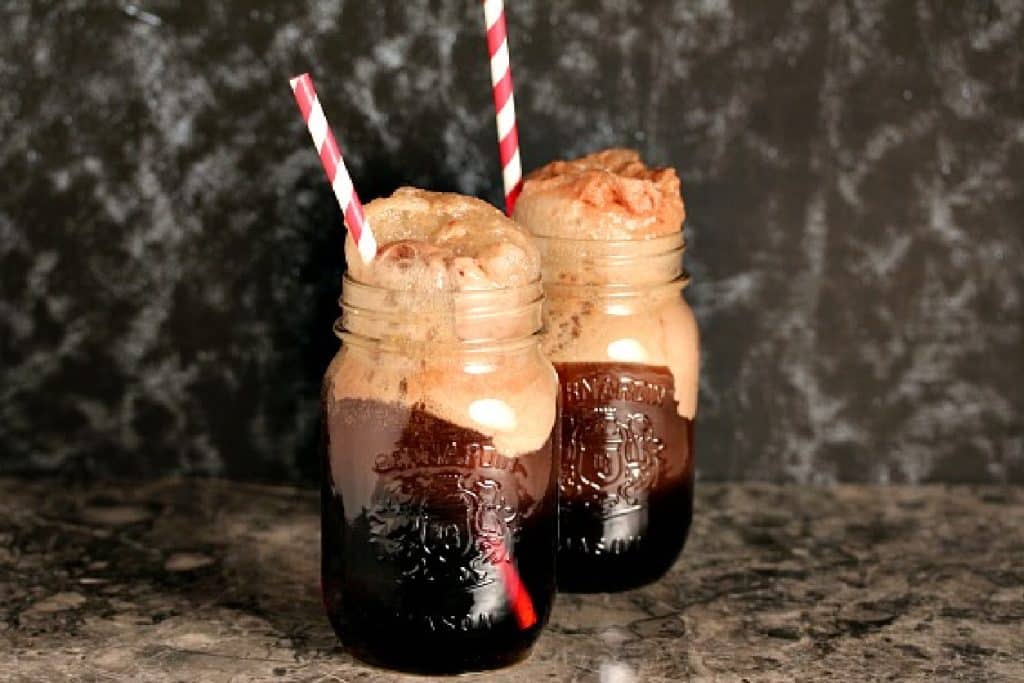 Two mason jars filled with cherry cola floats with straws in them on a counter. 