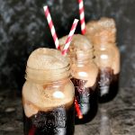 Three mason jars filled with cherry cola floats with straws in them on a counter.