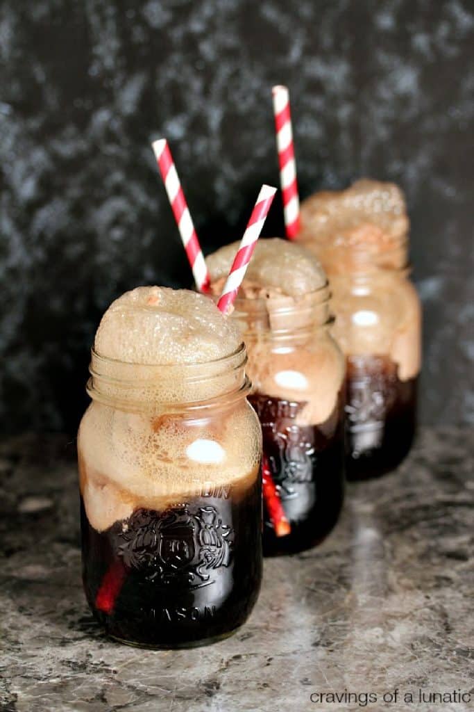 Three mason jars filled with cherry cola floats with straws in them on a counter. 