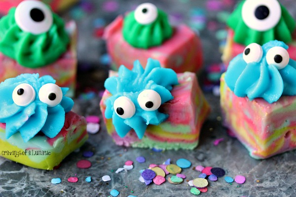 Easy Monster Fudge is brightly coloured swirled fudge cut into squares then topped with icing and googly eyes. Fudge is sitting a grey counter with colourful confetti all around it.