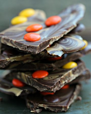 Peanut Butter and Chocolate Bark with Reese's Pieces stacked on a dark counter.