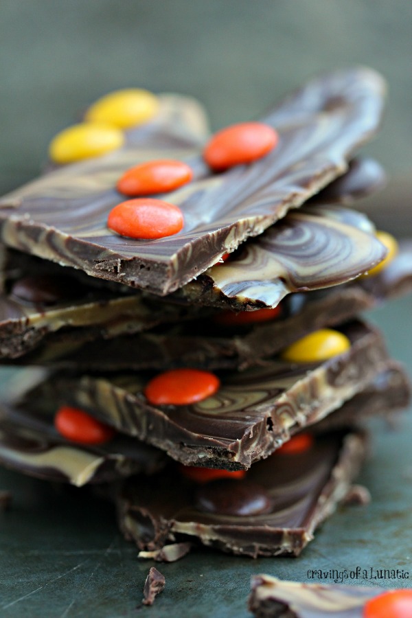 Peanut Butter and Chocolate Bark with Reese's Pieces stacked on a dark counter.