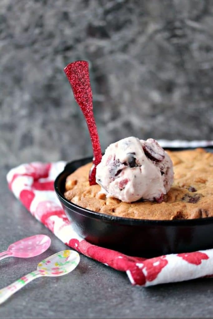 Chocolate peanut butter skillet cookie in a cast iron pan with ice cream on top and small colourful spoons in and around the cookie.