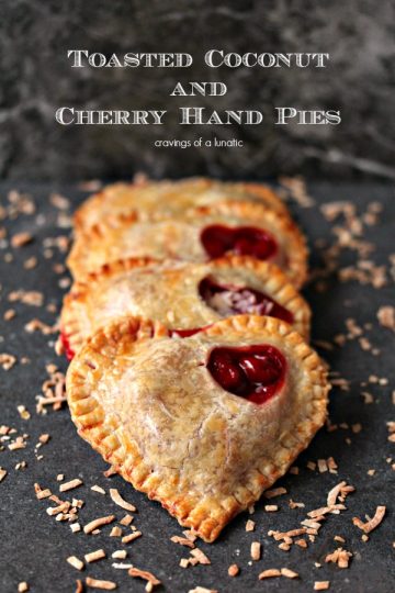 Toasted Coconut and Cherry Hand Pies stacked on a dark counter with toasted coconut scattered around them.