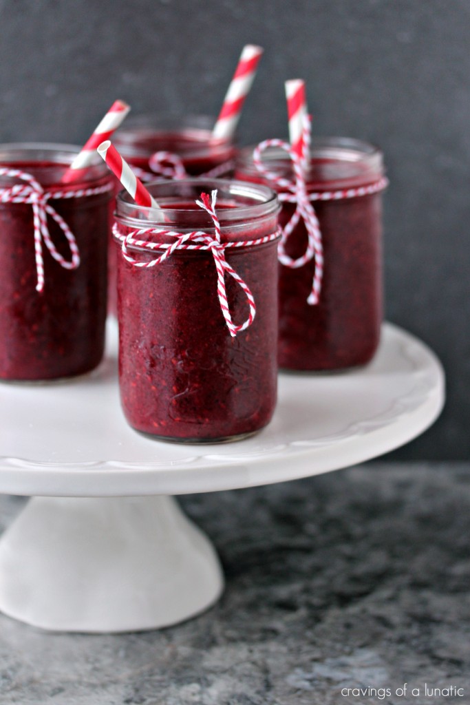 Mixed Berry Smoothie served in mason jars with twine tied on the rims and red and white straws in each glass, glasses are on a white cake stand.
