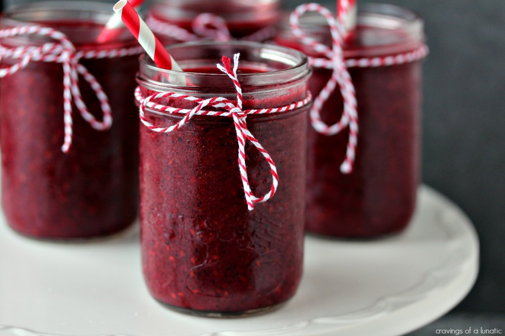 Mixed Berry Smoothie served in mason jars with twine tied on the rims and red and white straws in each glass, glasses are on a white cake stand.