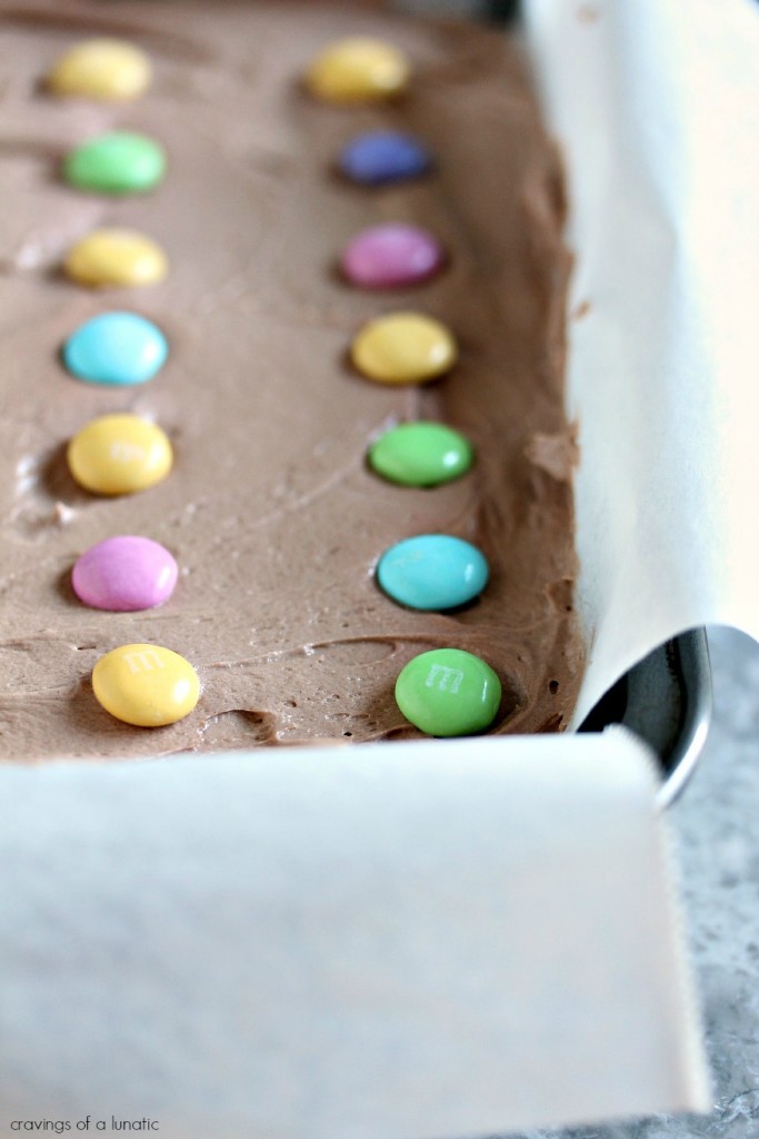 chocolate brownies with chocolate frosting and topped with M&M candies in a baking pan with parchment paper 