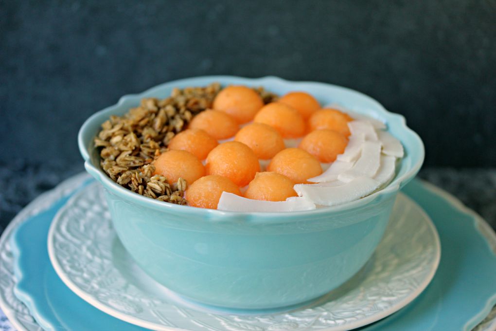 Cantaloupe Breakfast Bowl served in a blue bowl stacked on white and blue plates.