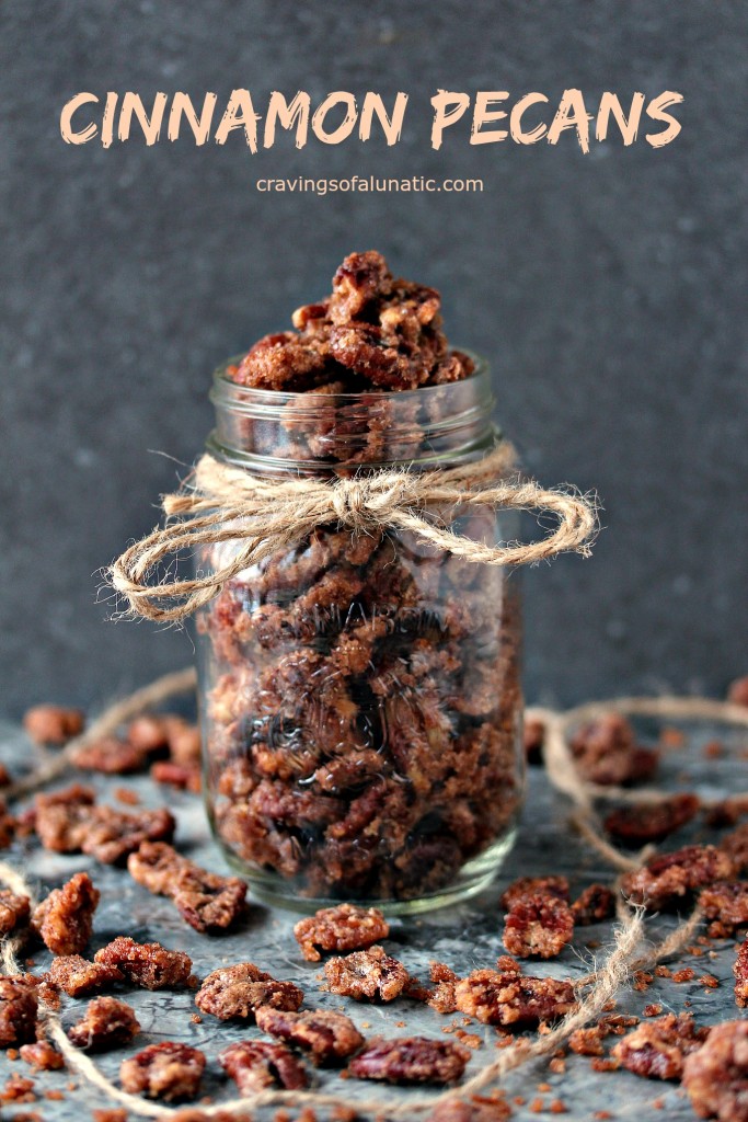 Cinnamon pecans in a mason jar with twine tied around the top and pecans scattered on a counter.