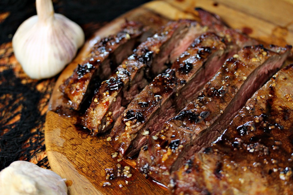 flank steak cooked to perfection resting on a wood board with garlic next to it