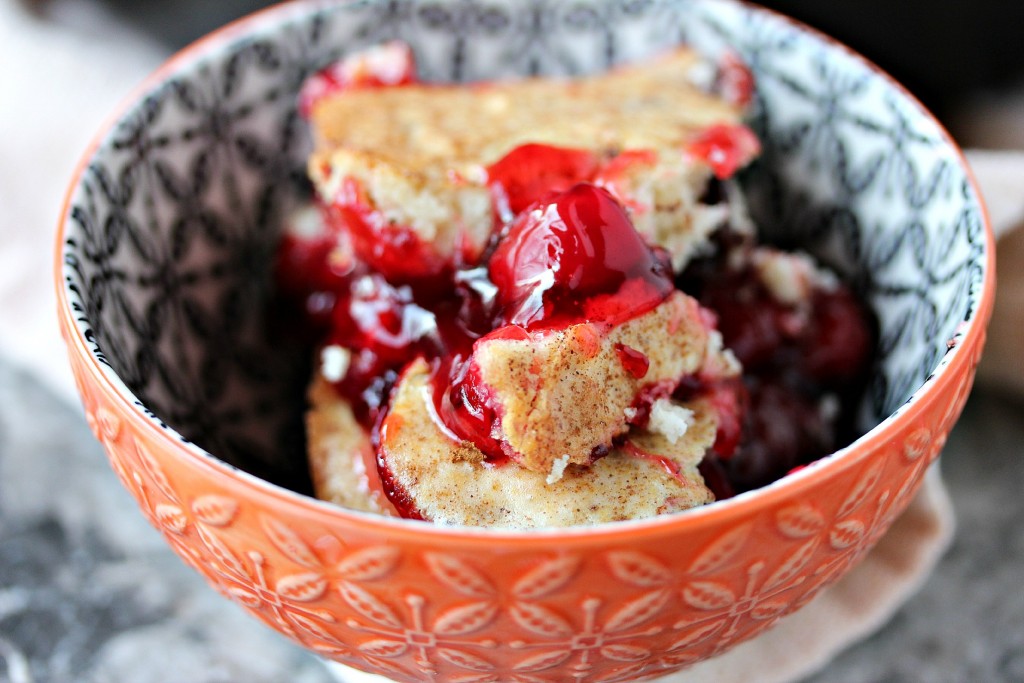 Close up image of cherry cobbler in a small orange bowl.