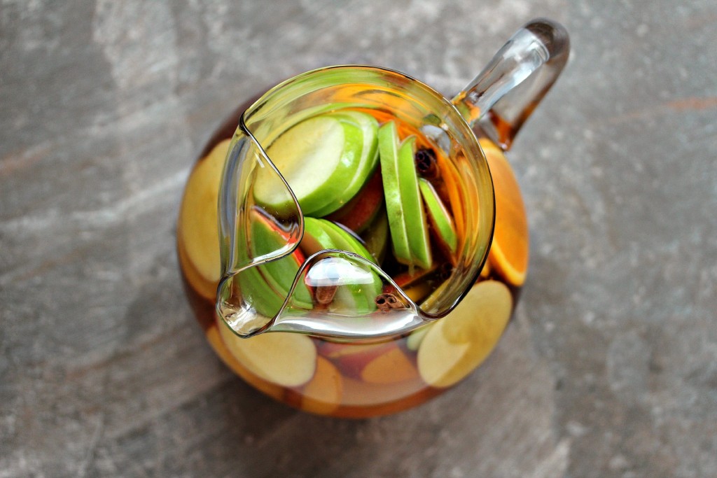 Overhead image of apple sangria in a clear glass pitcher on a neutral coloured countertop.