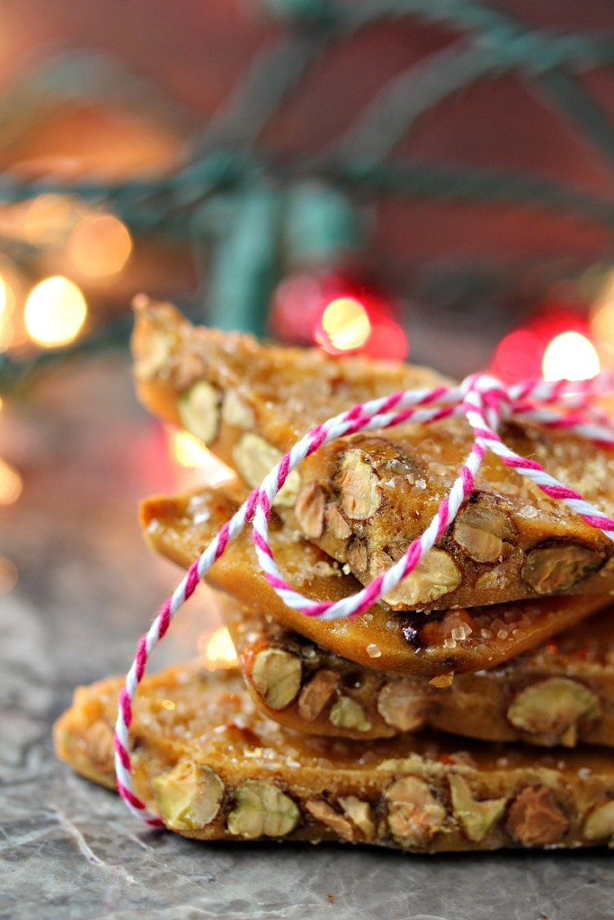 Microwave Pistachio Brittle stacked and tied with red and white twine with Christmas lights in the background.
