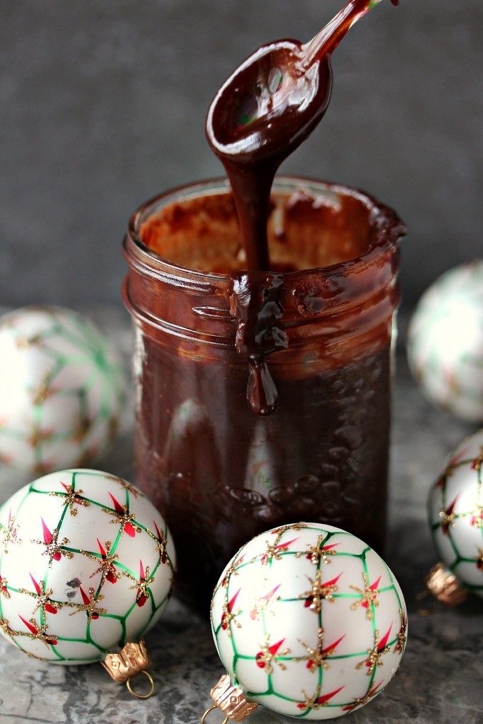 Nutella ganache in a mason jar with a spoonful of it being lifted out. Small holiday ornaments surround the jar. 