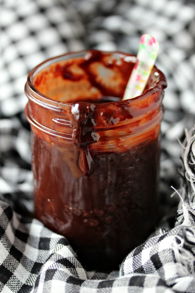 Nutella Ganache in a mason jar with a spoon it it, sitting on a black and white checkboard napkin. 