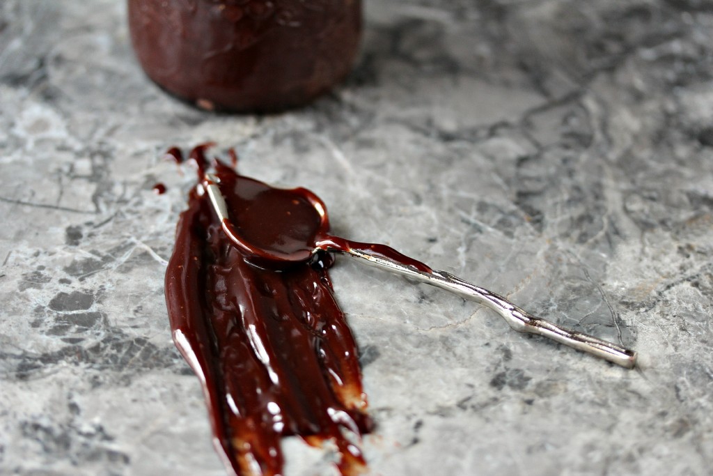 Nutella Ganache in a mason jar with a spoonful of it on a counter with a big mess by it. 