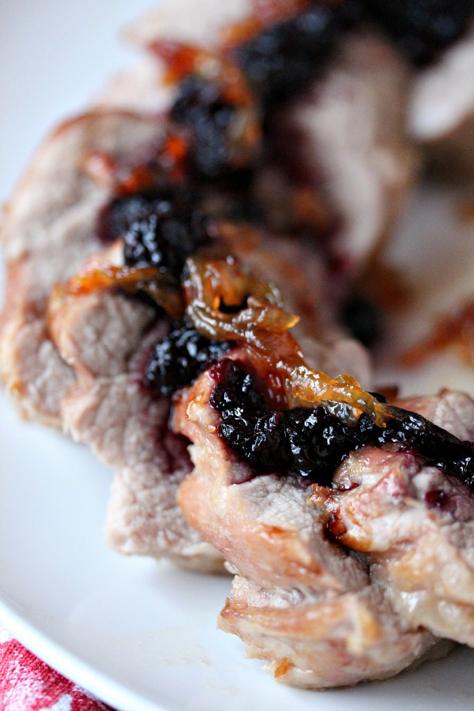 Pork Tenderloin cut int pieces with Haskapa Chutney and caramelized onions over top on a white plate.