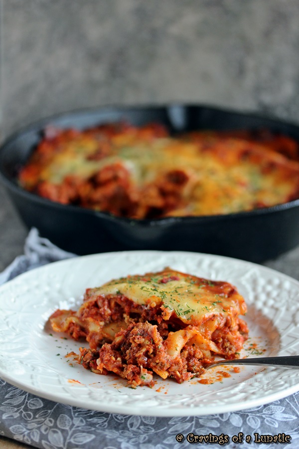 Skillet lasagna served on a white plate with cast iron skillet filled with lasagna in the background