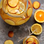 Peach Sangria served in a glass pitcher and mason jar with sliced peaches and sliced oranges