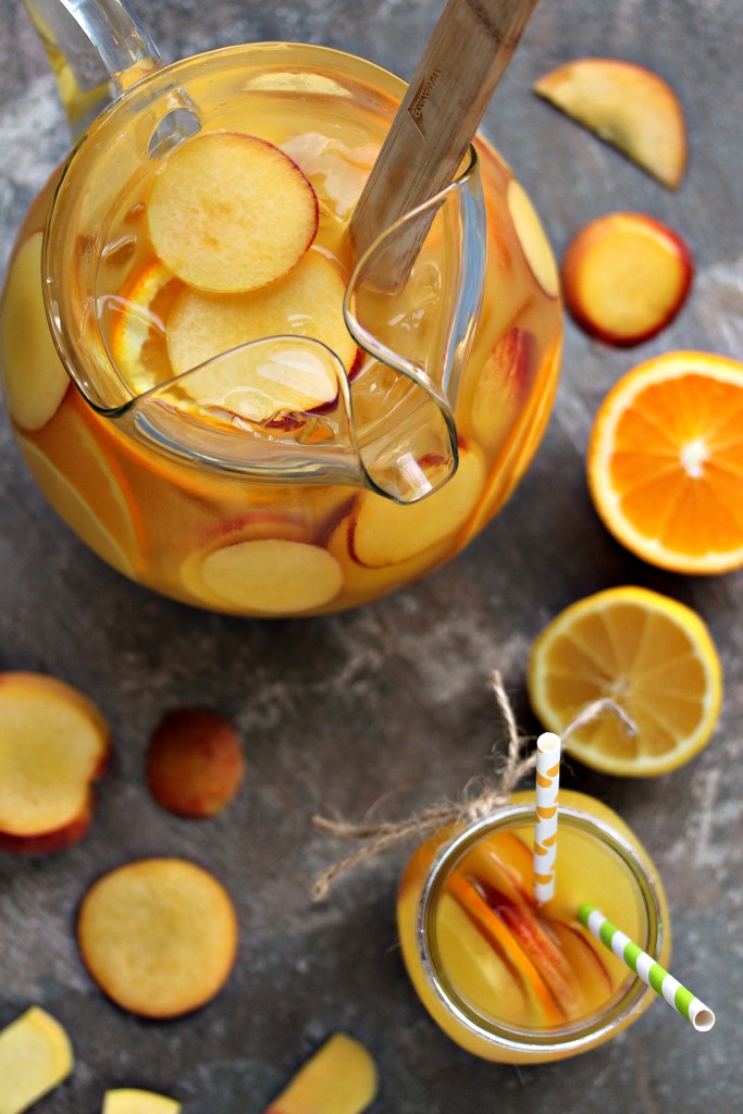Peach Sangria served in a glass pitcher and mason jar with sliced peaches and sliced oranges