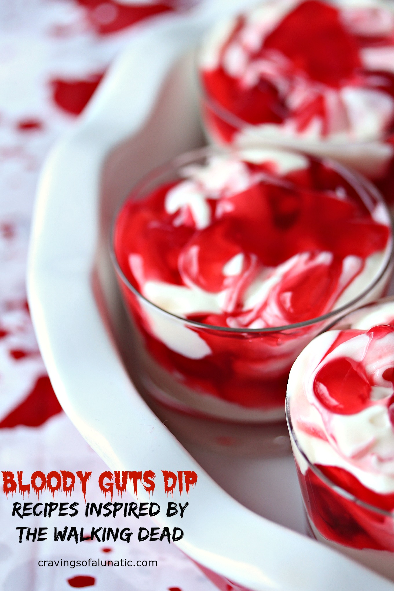 cherry cheesecake dip served in tiny glass serving dishes inside a red and white pan on a napkin with fake blood splatters on it