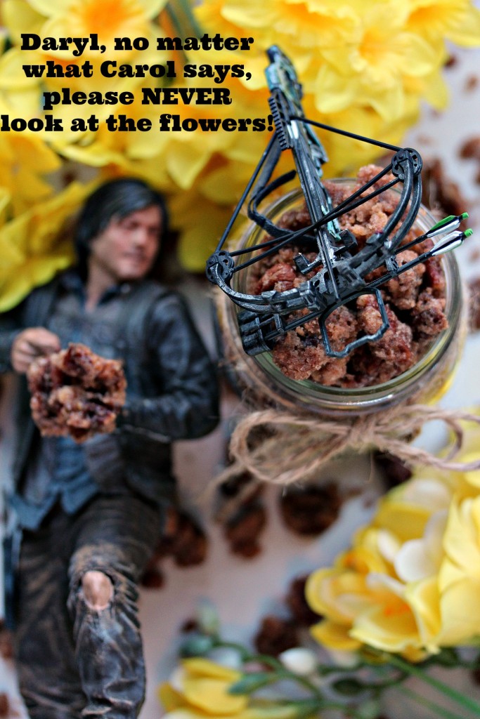 Cinnamon Pecans in a mason jar with twine tied around the top, pecans scattered around on a white surface with yellow flowers in two of the corners of the photo and a figurine of Daryl Dixon with his crossbow.